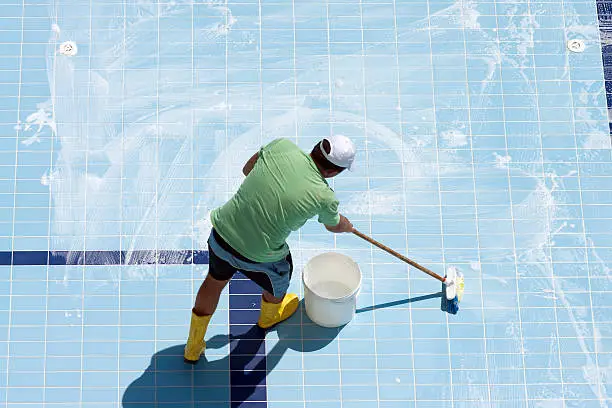Technician removing thick calcium buildup from pool tile beside an attached raised spa