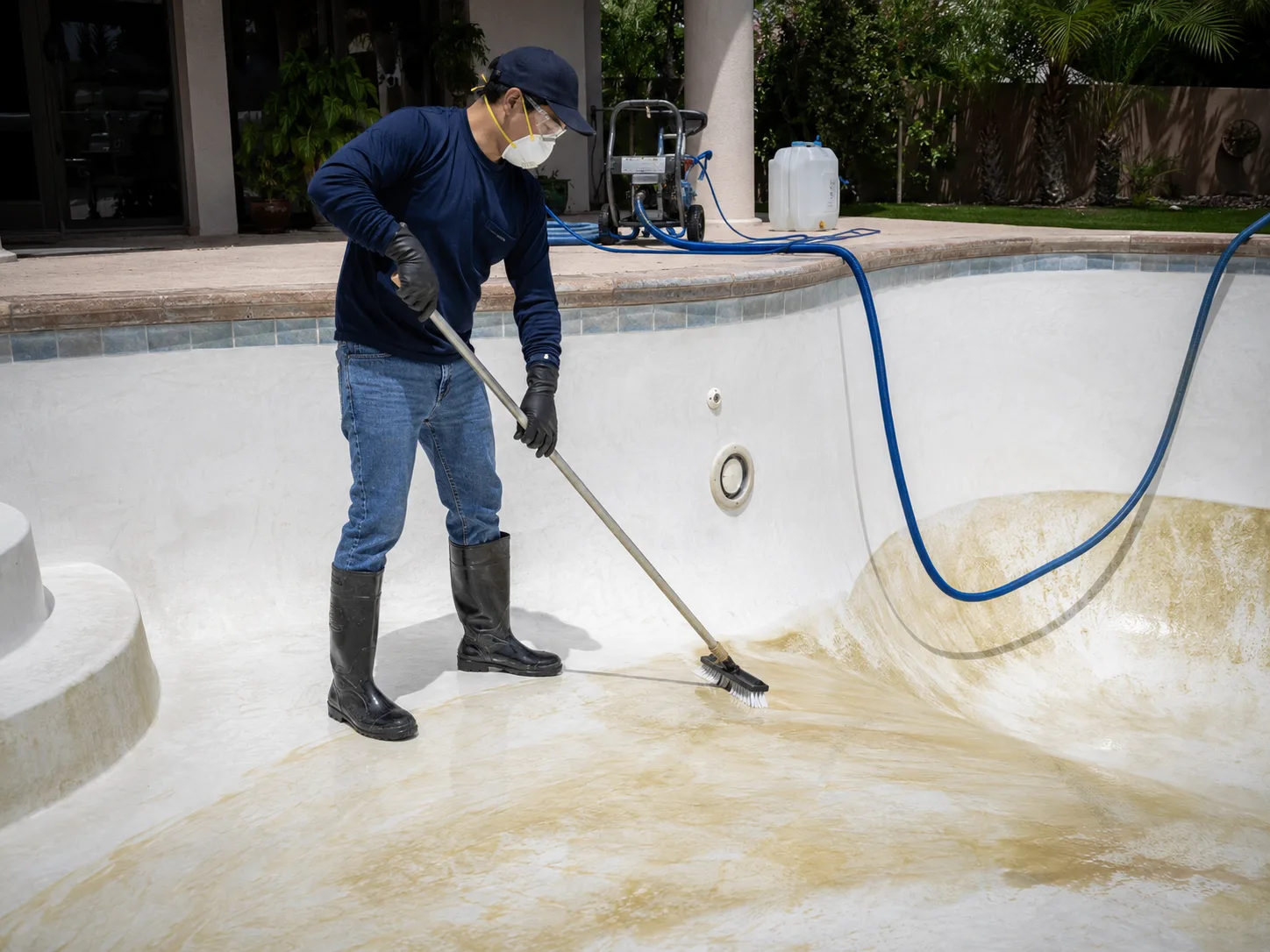 Technician acid washing stained plaster pool before summer backyard entertaining